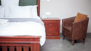 A bedroom with a wooden bed, a nightstand with a telephone, and a leather armchair.