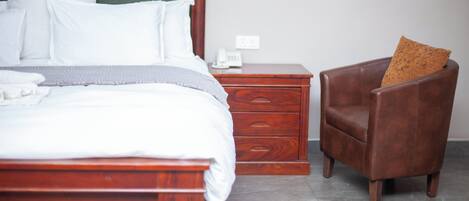 A bedroom with a wooden bed, a nightstand with a telephone, and a leather armchair.