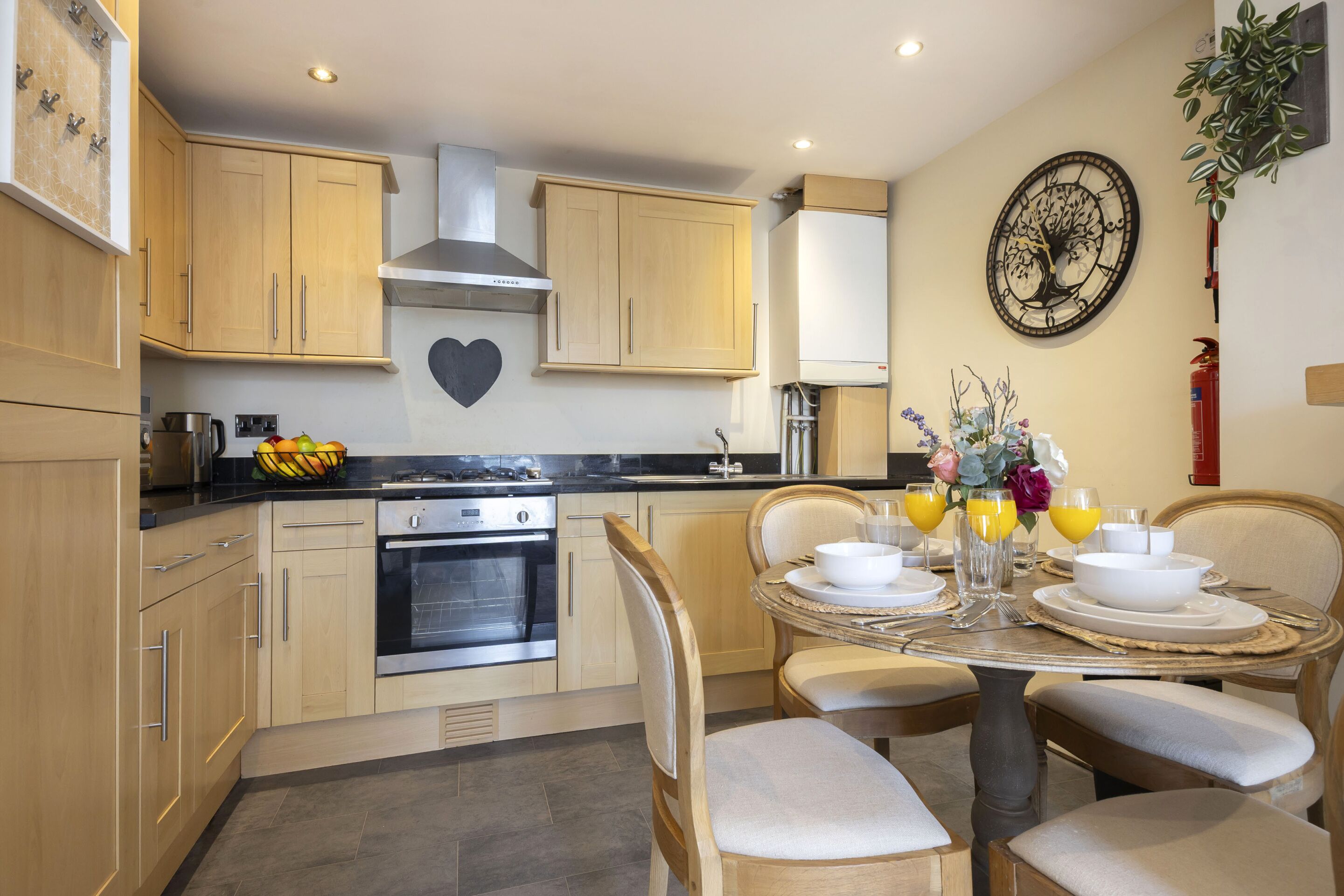 A modern kitchen with wooden cabinets, a stainless steel range hood, and a dining area with a table set for four.