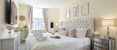 Une chambre élégamment aménagée, dotée d’un grand lit, de tables de chevet, d’un téléviseur et d’œuvres d’art encadrées accrochées au mur.