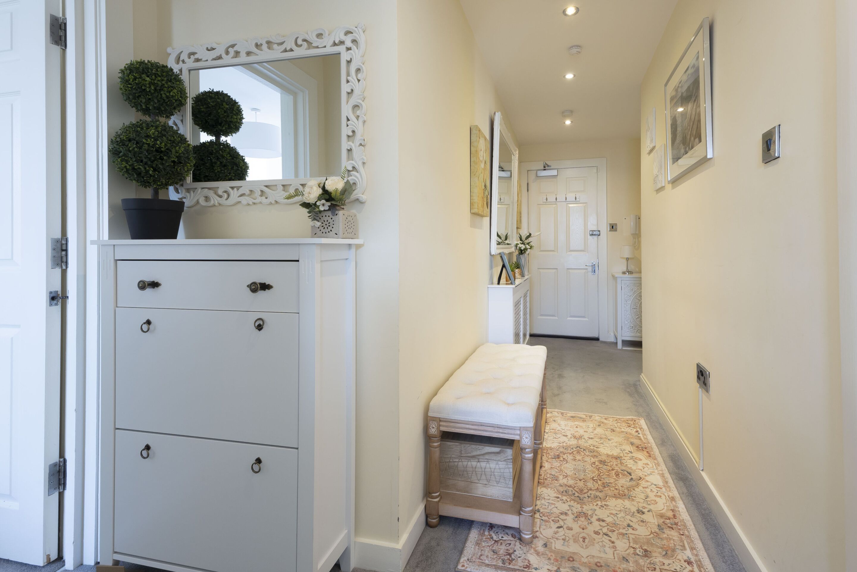 A hallway with a white cabinet, a bench, and a mirror with decorative foliage.