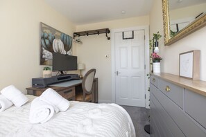 Ein Schlafzimmer mit Bett, Schreibtisch mit Computer, Stuhl, Kommode, Tür und einem Bild an der Wand.