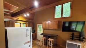 A kitchen with wooden cabinets, a refrigerator, a microwave, a bar stool, a television, and an air conditioning unit. - Convenient Lakeside House (Rangeley)