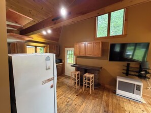Eine Küche mit Holzausstattung, einem Kühlschrank, einer Mikrowelle, einem Barhocker, einem Fernseher und einer Klimaanlage.