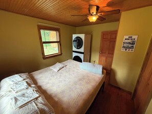 Ein Schlafzimmer mit einem Bett, einem Deckenventilator, einer Waschmaschine und einer Tür.