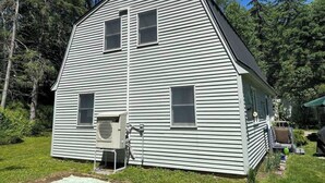 A two-story house with a central chimney, a small porch, and an air conditioning unit. - Convenient Lakeside House (Rangeley)