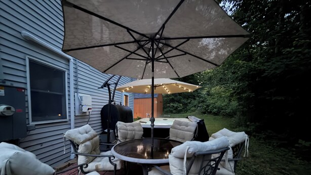 An outdoor patio with a round table, four chairs, and a large umbrella. - Convenient Lakeside House (Rangeley)