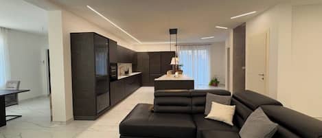 A modern living room with a sectional sofa, a dining area, and a kitchen.