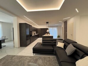 A modern living room with a sectional sofa, a dining area, and a kitchen.