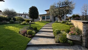 Un chemin de pierres mène à une maison dotée d’une pelouse bien entretenue et de diverses plantes.