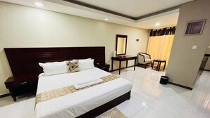 Habitación de hotel con una cama grande, una mesita de noche, una silla, una pequeña mesa y un espejo.