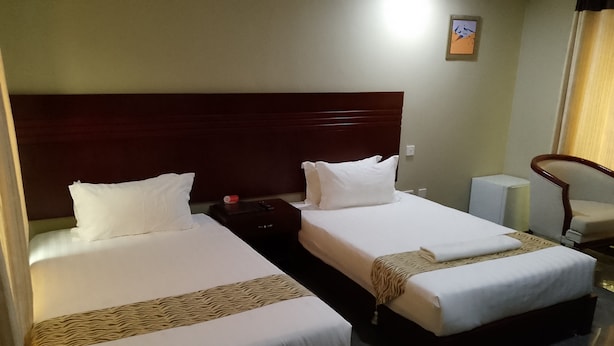 Habitación de hotel con dos camas, una mesita de noche, una silla y una pequeña mesa.