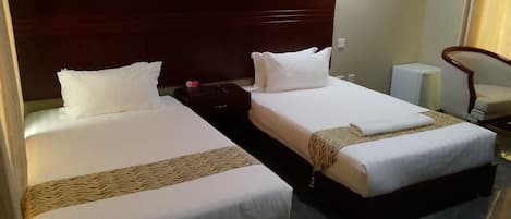 Habitación de hotel con dos camas, una mesita de noche, una silla y una pequeña mesa.