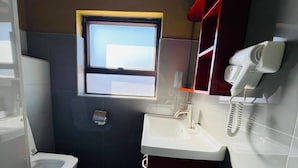Un baño pequeño con inodoro, lavamanos, ventana y secador de pelo fijado en la pared.