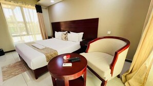 Habitación de hotel con cama, una silla, una mesita y ventana con cortinas.