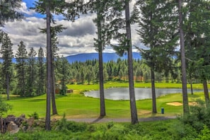 A golf course with a lake, surrounded by tall trees and mountains in the background. - 1PM In/Out | Play All Day / Soak All Night | GameRoom + Swim Spa (Cle Elum)