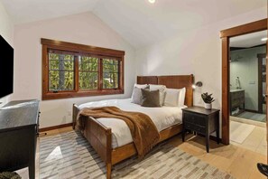 A bedroom with a bed, a nightstand, a window, and a door leading to a bathroom. - 1PM In/Out | Play All Day / Soak All Night | GameRoom + Swim Spa (Cle Elum)