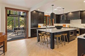 A modern kitchen with dark cabinetry, a central island with stools, and a view of the outdoors. - 1PM In/Out | Play All Day / Soak All Night | GameRoom + Swim Spa (Cle Elum)