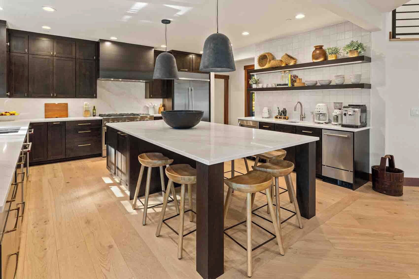 Cozinha moderna com armários escuros, uma ilha central com bancos, iluminação pendente e forno embutido.