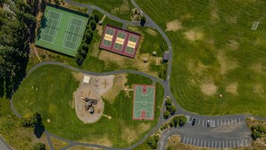 An aerial view of a sports complex with multiple tennis courts, a basketball court, and a parking area. - 1PM In/Out | Play All Day / Soak All Night | GameRoom + Swim Spa (Cle Elum)