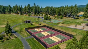 An aerial view of a golf course with multiple tennis courts, a parking area, and surrounding wooded areas. - 1PM In/Out | Play All Day / Soak All Night | GameRoom + Swim Spa (Cle Elum)