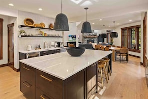 Una cocina moderna con una isla grande, iluminación colgante y un comedor con sillas de madera.
