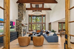 A spacious living room with a stone fireplace, large windows, and a high ceiling with exposed beams. - 1PM In/Out | Play All Day / Soak All Night | GameRoom + Swim Spa (Cle Elum)