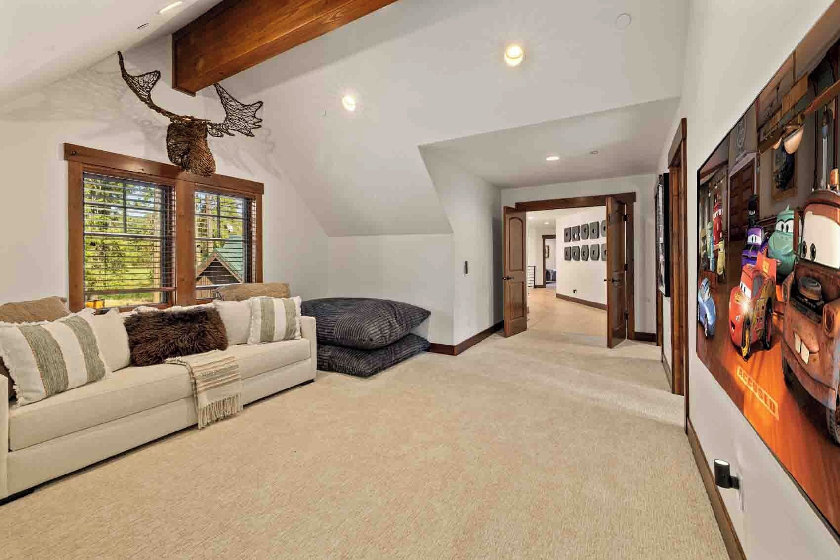 A spacious living room with a high ceiling, a large window, a sofa, and a wall-mounted display of animated characters.