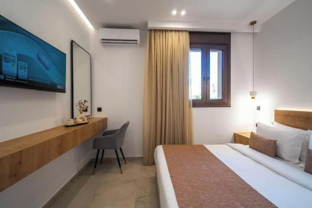 Ein modernes Hotelzimmer mit Bett, Schreibtisch, Stuhl, Wandfernseher und einem Vorhangfenster.