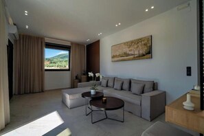 A modern living room with a sofa, two coffee tables, and a painting on the wall. - Irisma Luxury Villas • 2 Private Pools (Crete)