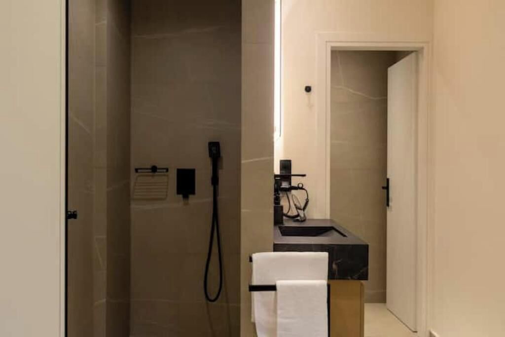 A modern bathroom with a glass shower enclosure, a black sink, and a towel rack.