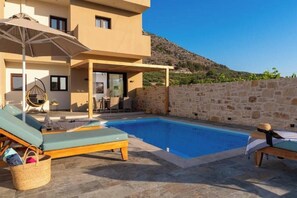 A pool area with lounge chairs and a table, surrounded by stone walls and a mountain backdrop. - Irisma Luxury Villas • 2 Private Pools (Crete)