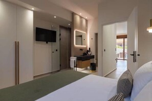 Une chambre d’hôtel moderne, équipée d’un lit, d’un téléviseur fixé au mur, d’une salle de bain avec un miroir et d’un couloir menant à une autre chambre.