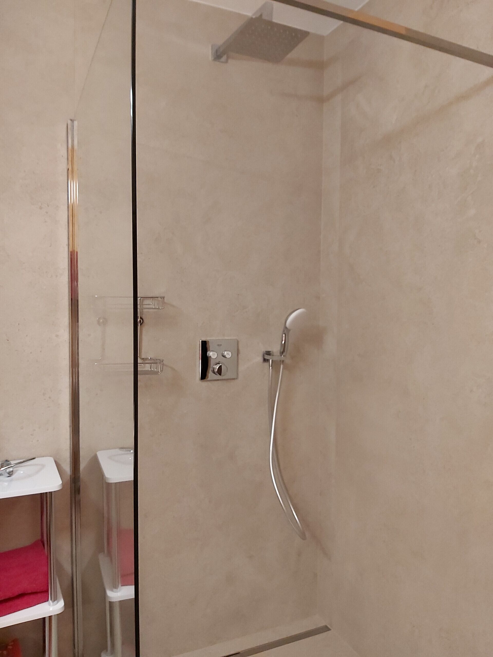 A glass-enclosed shower with a handheld showerhead and a wall-mounted control panel.