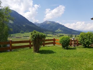 A wooden fence with a small house and a tree in a grassy field with mountains in the background. - Apartment Sibylle by Alpine Host Helpers (Kirchberg in Tirol)