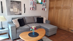 A grey sectional sofa with black and white cushions, a wooden coffee table with a vase of flowers, a lamp, and a wall with decorative elements. - Apartment Sibylle by Alpine Host Helpers (Kirchberg in Tirol)