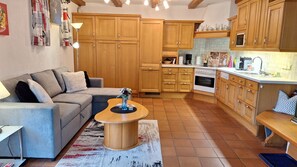 Een woonkamer met een grijze bank, een salontafel en een keuken met houten kasten en een betegelde spatwand.