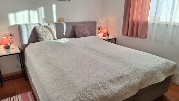 A neatly made bed with a white quilt, two bedside tables with lamps, and a window with curtains. - Apartment Sibylle by Alpine Host Helpers (Kirchberg in Tirol)