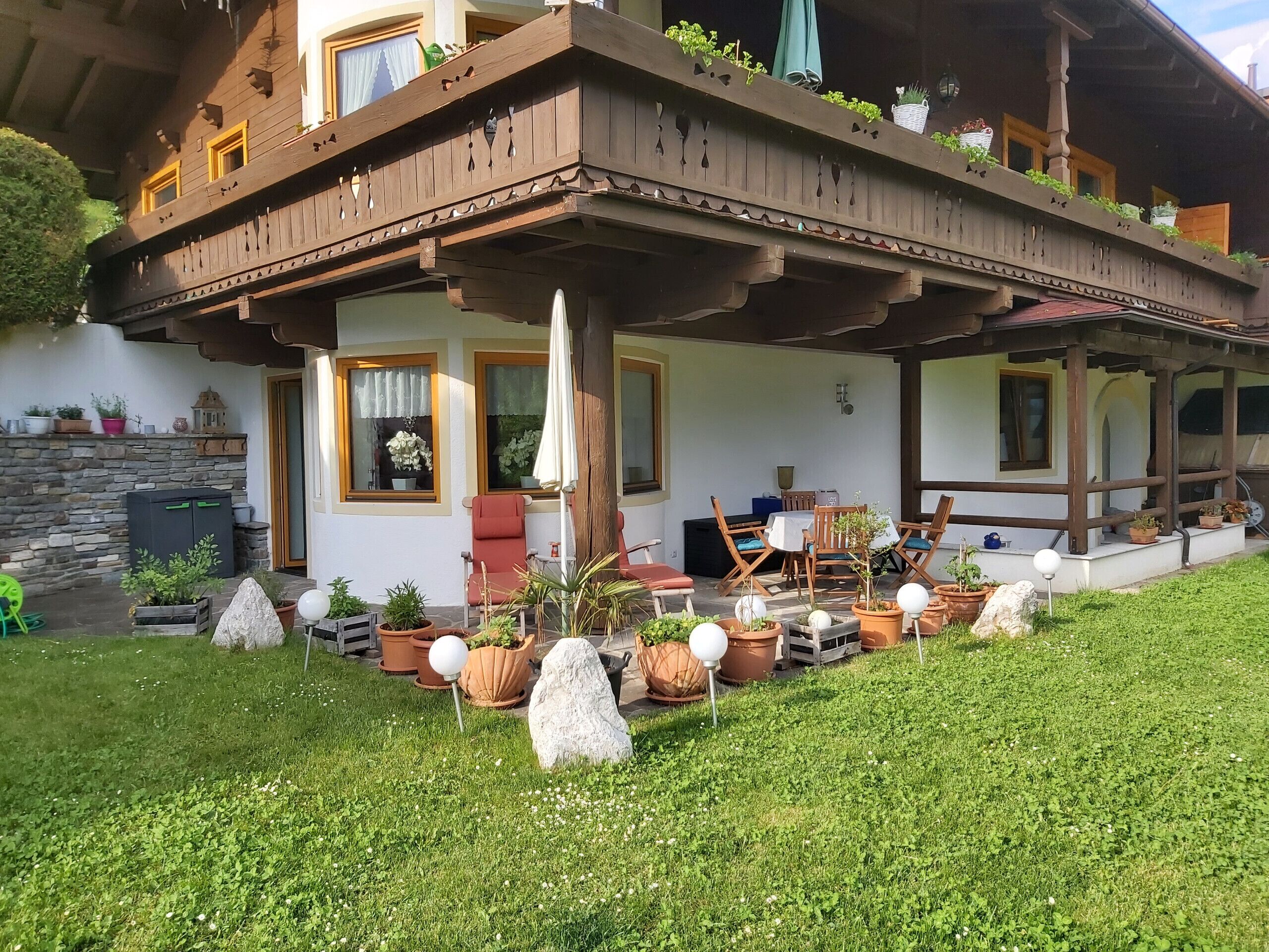 Eine Chalet mit Holzbalkon, Sitzgelegenheit im Freien und Topfpflanzen.
