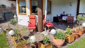 A covered outdoor seating area with wooden chairs and tables, surrounded by potted plants and a stone floor. - Apartment Sibylle by Alpine Host Helpers (Kirchberg in Tirol)