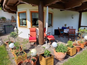 A covered outdoor seating area with wooden chairs and tables, surrounded by potted plants and a stone floor. - Apartment Sibylle by Alpine Host Helpers (Kirchberg in Tirol)