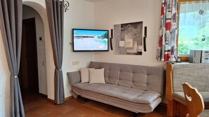 A living room with a sofa, a television mounted on the wall, and a window with curtains. - Apartment Sibylle by Alpine Host Helpers (Kirchberg in Tirol)