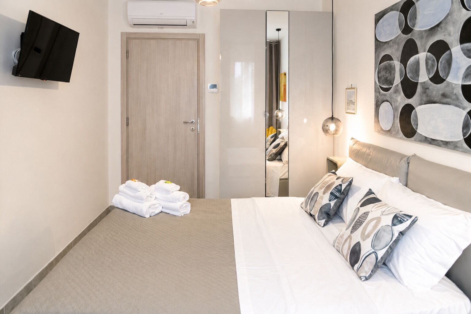 Una habitació d'hotel amb un llit, una televisió de pantalla plana, un mirall i un quadre a la paret.