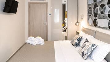 A hotel room with a bed, a flat-screen TV, a mirror, and a painting on the wall.