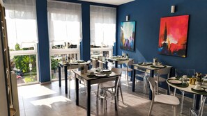 A dining area with tables set for service, large windows with sheer curtains, and abstract art on the walls. - Hotiday Ferrara Centro (Ferrara)