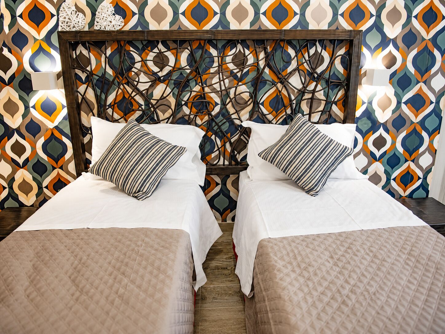 A double bed with a wooden headboard and two pillows, set against a patterned wall.