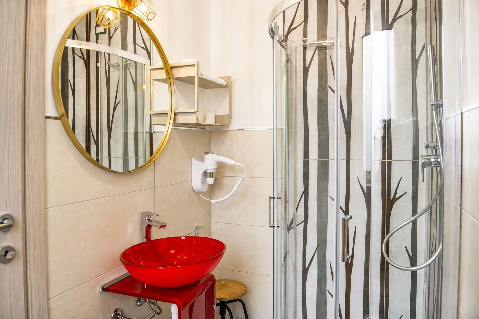 A bathroom with a glass shower enclosure, a red sink, and a wall-mounted mirror.