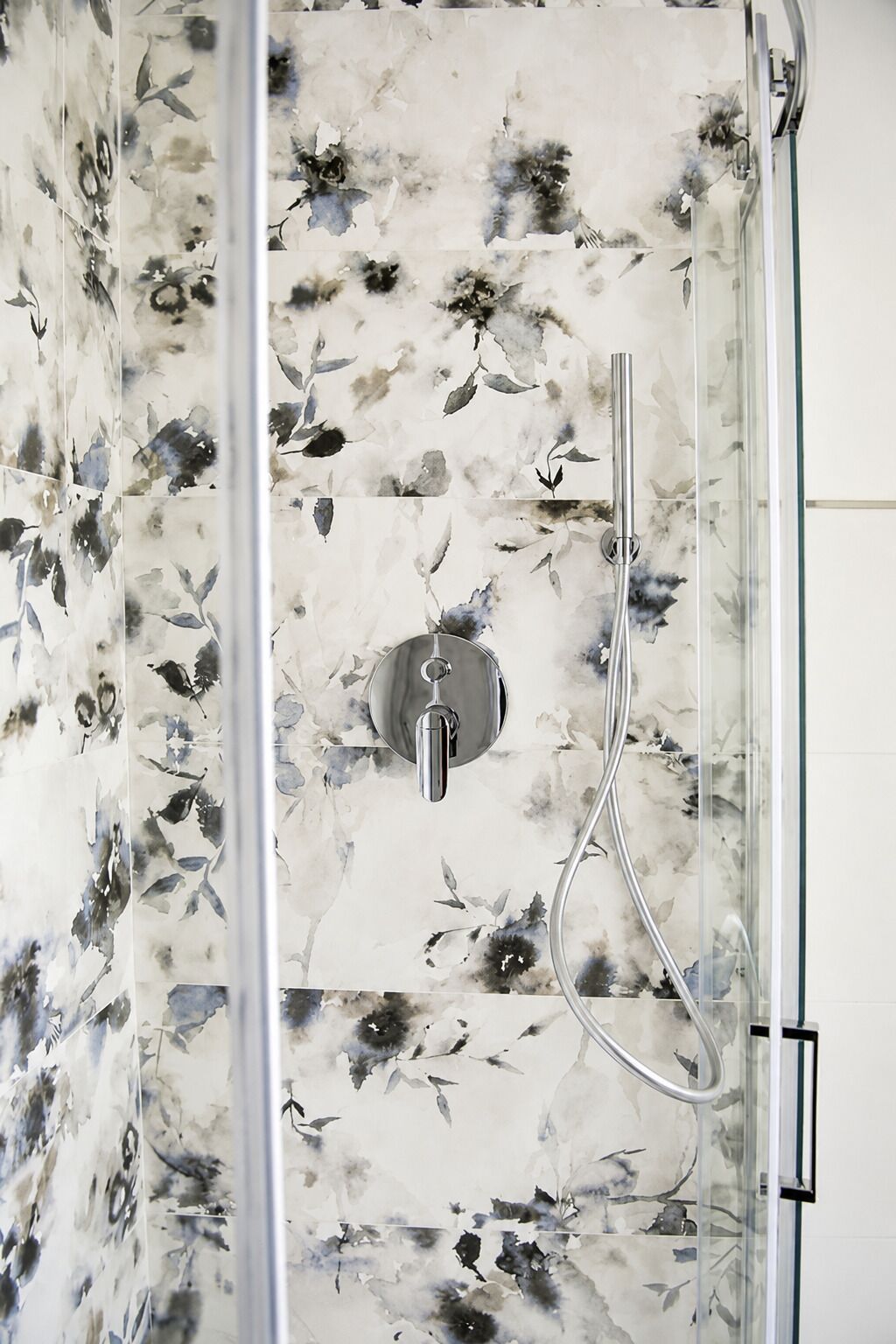 Eine Dusche mit einem Blumenmuster an den Fliesen und einem Chrom-Wasserhahn.
