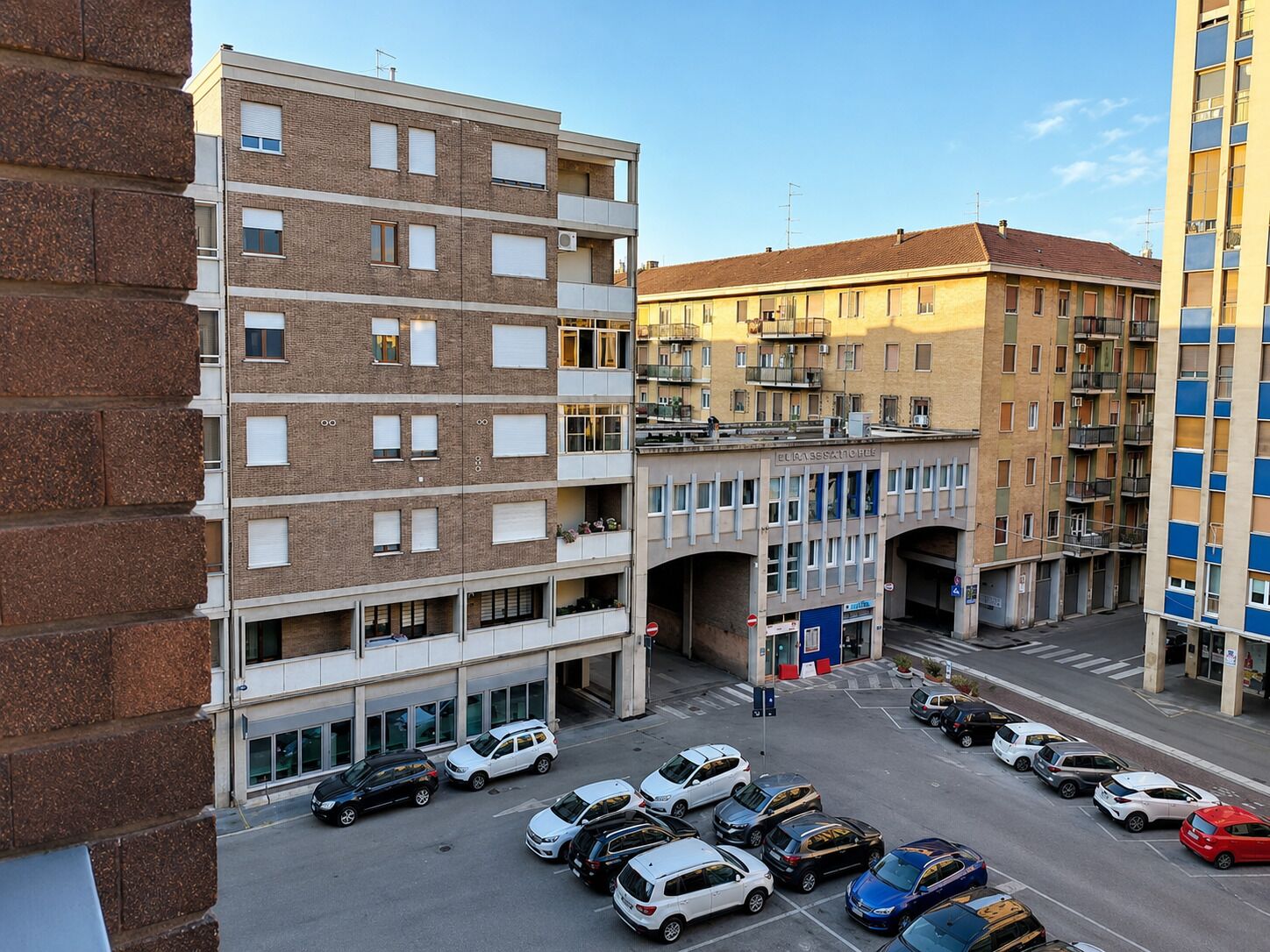 Un parcheggio multipiano con diverse auto parcheggiate, un edificio con balconi e cielo sereno.