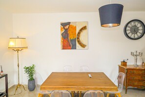 Un comedor con una mesa de madera, sillas, una lámpara, un reloj y un cuadro en la pared.